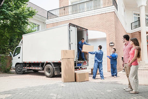 young couple watching movers move boxes from the moving van